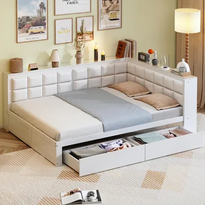 A white corner daybed with storage drawers is shown in a room with decorative pictures on the wall and a floor lamp.