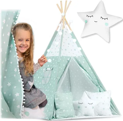 A young girl peeking out from behind a green and white star-patterned teepee tent, with star-shaped pillows inside.