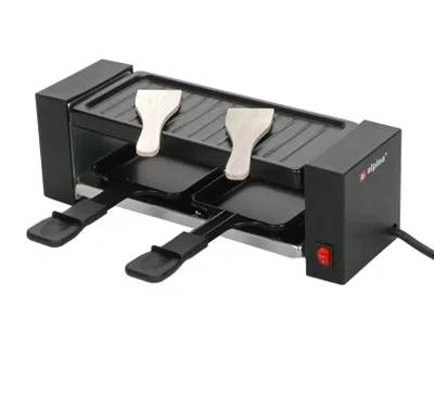 A black electric raclette grill with two wooden spatulas on top and two black raclette pans underneath, set against a white background.