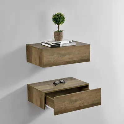 Two wooden floating shelves mounted on a light gray wall. The top shelf has books and a small potted plant. The bottom shelf has a pair of sunglasses and an open drawer.