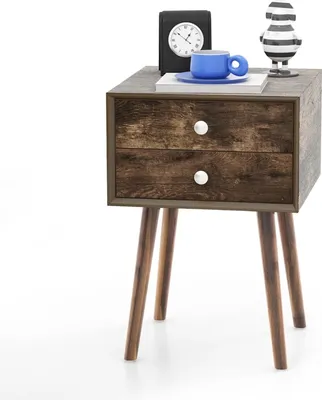 A wooden nightstand with two drawers and tapered legs, decorated with a clock, a blue coffee cup on a saucer, and a small figurine.