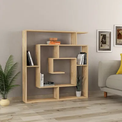 A modern wooden bookshelf is placed against a light gray wall, with a sofa and framed pictures visible in the background.