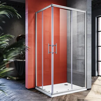 A modern bathroom with a red accent wall, featuring a glass shower enclosure with silver frames and double sliding doors. A large potted plant is in the foreground, and a bathtub is visible in the background.