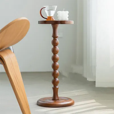 A small wooden side table with a glass cup and a candle on top, next to a wooden chair.