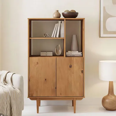 A wooden cabinet with shelves and doors, decorated with vases and books, placed in a living room setting next to a sofa and a lamp.