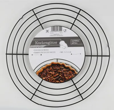 A round black metal cake cooling rack is shown against a white background. A circular label is attached to the center of the rack, displaying product information and an image of a pie.