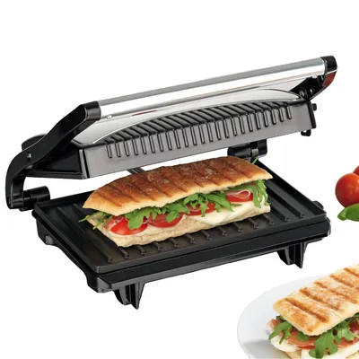 A panini press with a sandwich inside, and a second sandwich on a plate in the foreground.