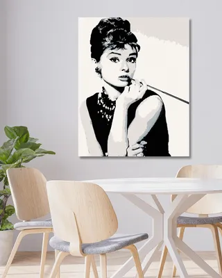 A diamond painting of Audrey Hepburn is displayed on a wall above a dining table with chairs.