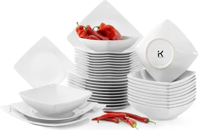 A collection of white square ceramic plates and bowls, some stacked, with red chili peppers placed in front and on top of some of the dishes.