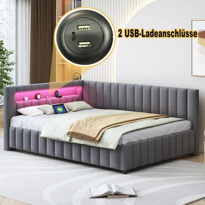 A grey upholstered bed with a built-in headboard shelf featuring pink LED lighting, a tablet, and decorative items. A close-up inset shows USB charging ports.