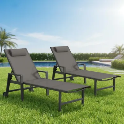 Two grey lounge chairs are set up on a green lawn next to a swimming pool on a sunny day.