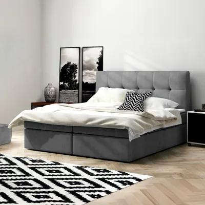 A bedroom scene featuring a bed with bedding and pillows, a rug, and artwork on the wall.