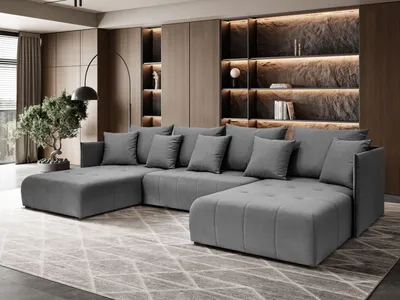 A modern living room with a large U-shaped sectional sofa in dark gray, placed on a patterned rug. The background features built-in shelving with ambient lighting and decorative items.