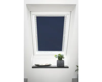 A dark blue roller blind is installed in a slanted window, with a small plant and a decorative bowl on a shelf below.