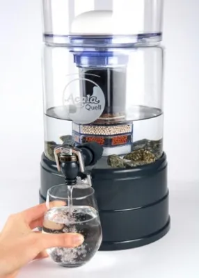 A hand is holding a glass under a water filter dispenser, filling it with water.