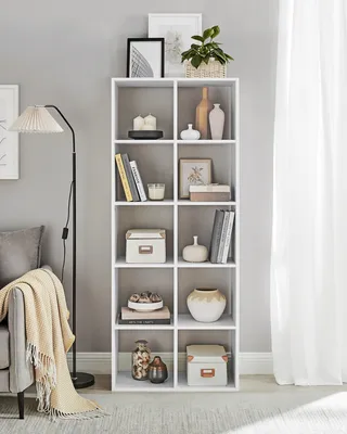 A white shelving unit filled with decorative items, books, and storage boxes, next to a sofa and a floor lamp.