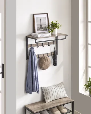 A wall-mounted coat rack with a shelf above it, displaying a shirt, a hat, and an umbrella on the hooks, and a framed picture and a plant on the shelf.