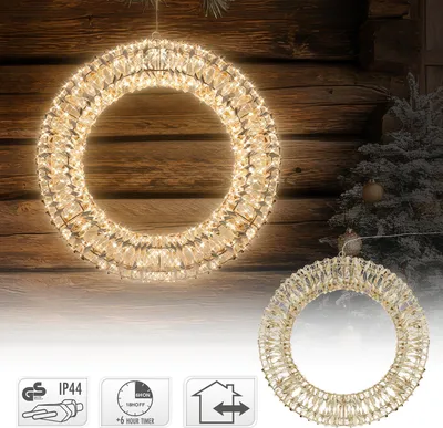A decorative LED Christmas wreath is displayed against a rustic wooden background, with a frosted Christmas tree and ornaments visible in the background. Several icons indicating product features are shown at the bottom.