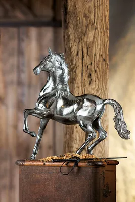 A silver-colored aluminum horse figurine is displayed on a wooden surface against a rustic wooden background.