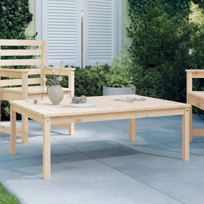 A wooden coffee table and chairs are set up on a patio with plants and shutters in the background.