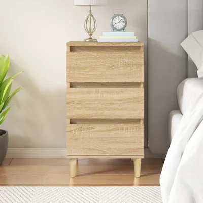 A bedside table with three drawers next to a bed.