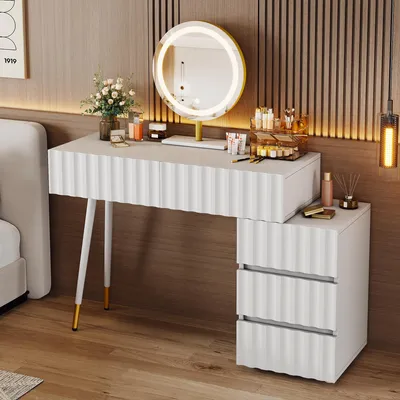 A white vanity table with a round LED mirror and makeup accessories is set up in a bedroom next to a bed.