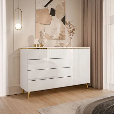 A white high-gloss dresser with gold accents and legs, placed in a room with a painting on the wall and curtains in the background.