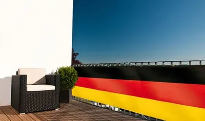 A balcony with a chair, a plant, and a German flag-themed balcony screen.