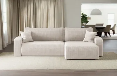 A beige sectional sofa is shown in a living room setting with curtains in the background and a dining area visible through an opening.