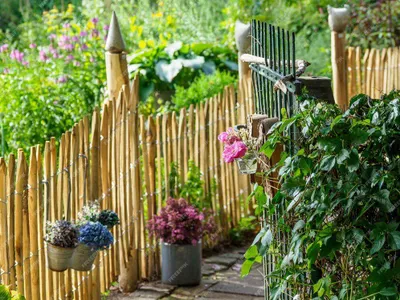 A rustic garden fence made of wooden stakes, with hanging flower pots and lush greenery.