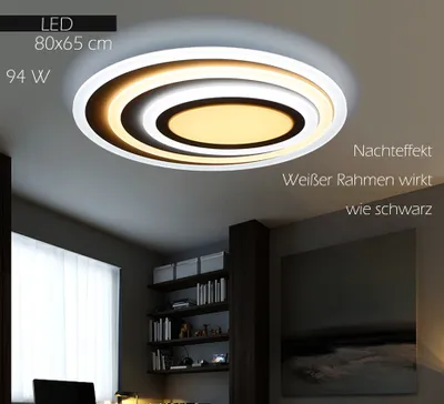 A modern ceiling light fixture with multiple concentric rings, illuminated in a warm yellow and white light, installed on a ceiling in a room with bookshelves and a painting.