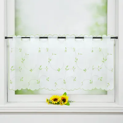 A white sheer curtain with green leaf embroidery hangs on a window rod, with two sunflowers on the windowsill below.