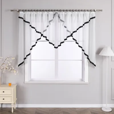A window with sheer white curtains trimmed with black ribbon, set in a room with a nightstand and a floor lamp.