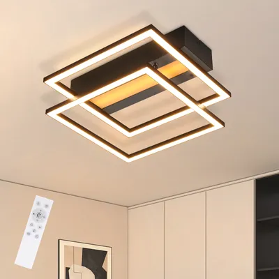 A modern, square-shaped LED ceiling light fixture with multiple interlocking frames, illuminated with white and warm yellow light, mounted on a white ceiling. A white remote control is visible in the lower-left corner.