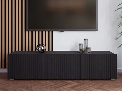 A black TV cabinet with decorative items on top, placed in front of a wall with wooden slats and a mounted television.