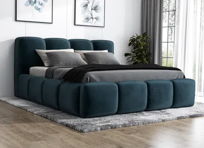 A dark blue upholstered bed with a tufted headboard and frame, set on a gray rug in a room with artwork on the wall and a plant near the window.