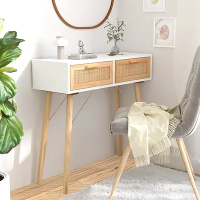 A console table with two rattan drawers is placed against a white wall, next to a chair with a blanket draped over it. A large plant is visible on the left side of the image.
