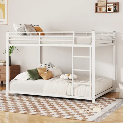 A white metal bunk bed with mattresses and pillows in a bedroom setting.