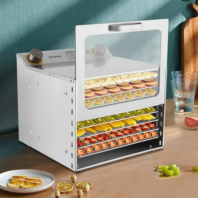 A stainless steel food dehydrator filled with various dried fruits and vegetables, placed on a wooden countertop.