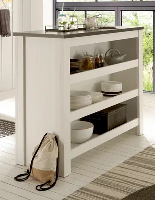 A white kitchen island with shelves filled with dishes and jars, set in a bright, modern kitchen with large windows.