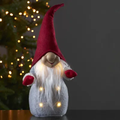 A festive gnome decoration with lights, placed in front of a blurred Christmas tree.