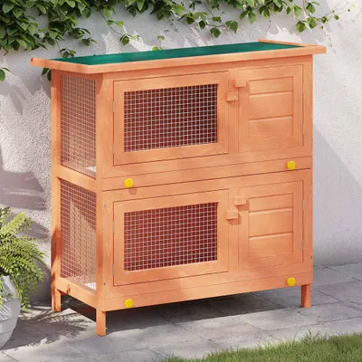 A two-tiered wooden rabbit hutch with green roof, set outdoors on a paved patio with grass and a wall with ivy in the background.