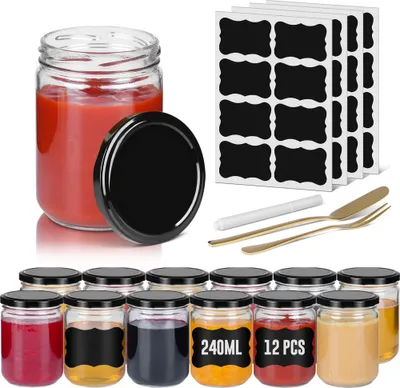 A collection of small glass jars with black lids, some filled with colorful contents, arranged on a white background. There are also sheets of black labels and a small white pen and gold cutlery in the background.