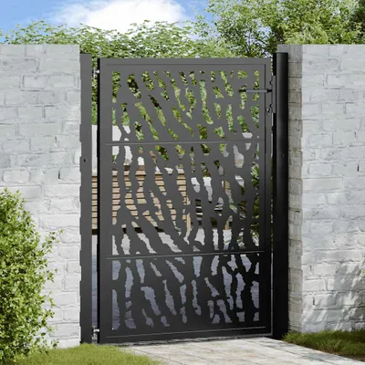 A black metal garden gate with a decorative cutout pattern, set against a white brick wall and greenery.