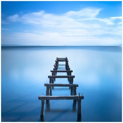 Produktbild von Wallario Premium Glasbild, freischwebende Optik, kräftige Farben, Größe 50 x 50 cm Motiv Rustikaler Holzsteg im blauen See