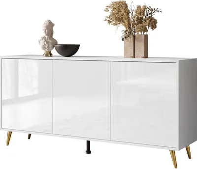 A white high-gloss sideboard with gold legs, decorated with a bust, a bowl, and a vase of dried flowers.