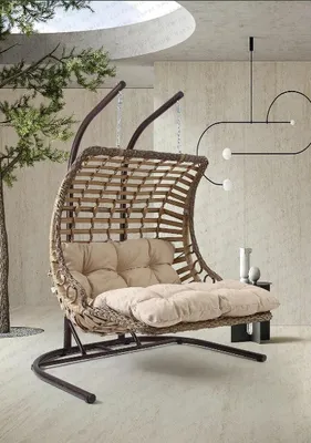 A hanging chair with cushions is shown in a modern indoor setting with a tree and abstract wall art.
