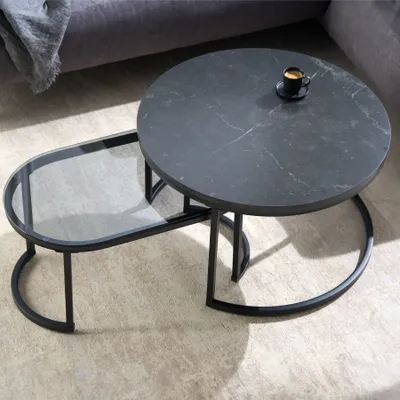 A coffee table set with a round top and an oval glass shelf, placed on a floor next to a sofa.