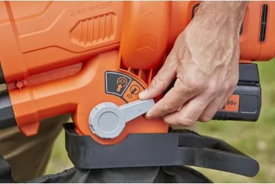 A hand is shown adjusting a dial on an orange leaf blower.