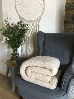 A folded blanket is placed on a chair next to a vase of flowers and a macrame wall hanging.